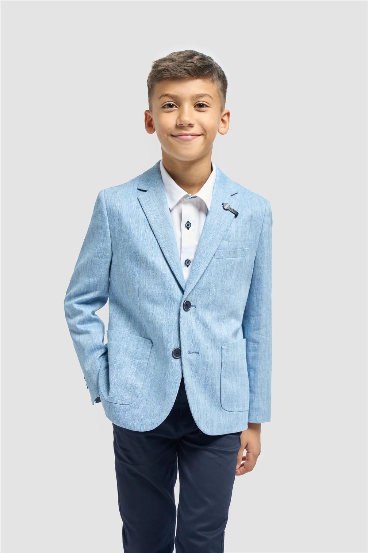 Young boy wearing a light blue blazer and dark pants on a white background