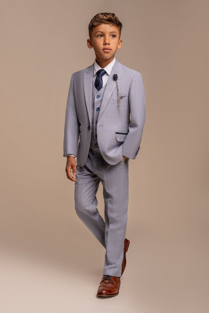 A boy wearing a sky blue three-piece suit with a white shirt and a dark tie, standing against a neutral background.